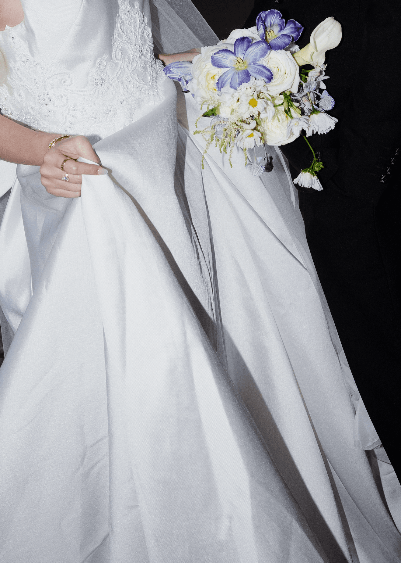 Bride holding a white and purple bouquet with her ring visible